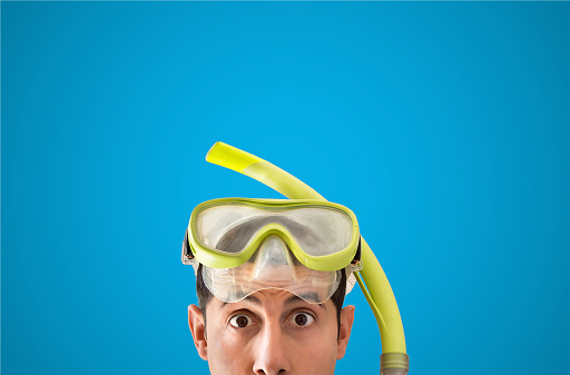 close up of man with snorkel mask looks surprised with blue background