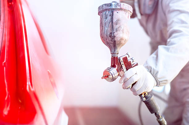 Close-up of spray gun with red paint painting a car stock photo