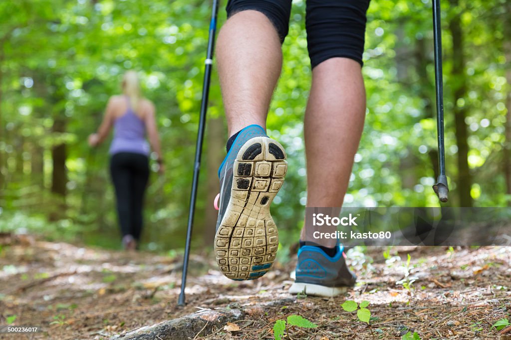 Young couple hiking in nature. Sport and exercise. Young fit couple hiking in nature. Adventure, sport and exercise. Detail of male step, legs and nordic walking poles in green woods. Nordic Walking Stock Photo