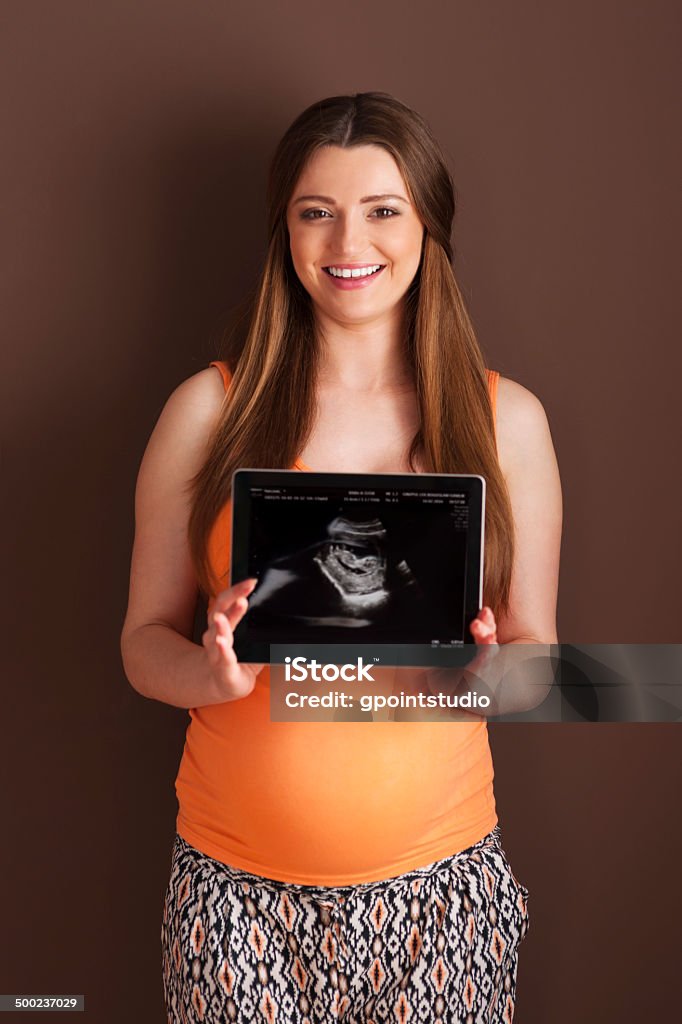 Beautiful pregnant woman showing ultrasound scan on digital tablet Adult Stock Photo