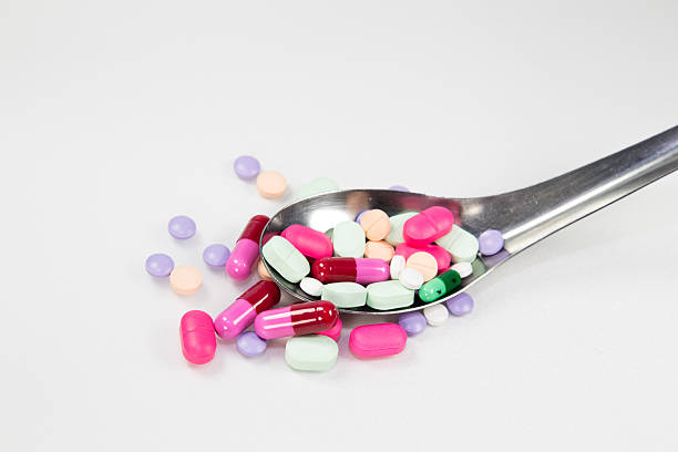 красочные таблетки, капсулы с ложкой на белом фоне - capsule vitamin pill red lecithin стоковые фото и изображения
