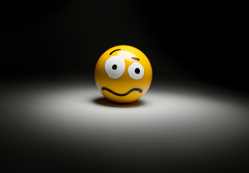 A 3D rendering of a yellow emoji face with rolling eyes isolated on a blue background