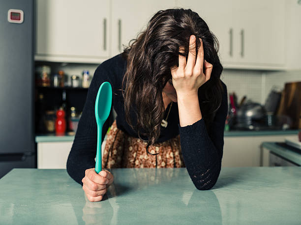 traurige frau mit löffel in der küche - mit dem kopf gegen die wand rennen stock-fotos und bilder