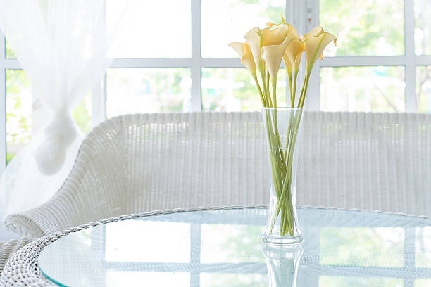 Yellow flower in vase on table and window sill background.