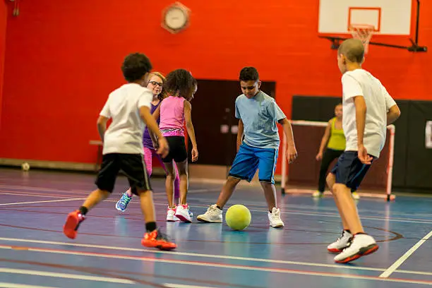 Kids playing soccer in gym class.