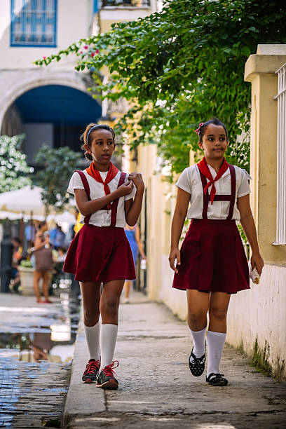 Havana, Cuba - November 6, 2015: Plaza Vieja in Old Havana on busy week day in November. Two school girls having a break and walking on the street. They both have school uniforms, typical for Cuban Government school system. Other people in the background. Seeing a happy group of young uniformed students is one of iconic sites visitors of Havana can experience anywhere in the city. Happy faces of new Cuban generation to come.
