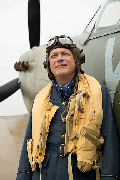 World War Two RAF fighter pilot looking up to the skies whilst leaning against the fuselage of his Spitfire aircraft. The Pilot Officer is wearing the  C-type flying helmet and "Mae West" life jacket.