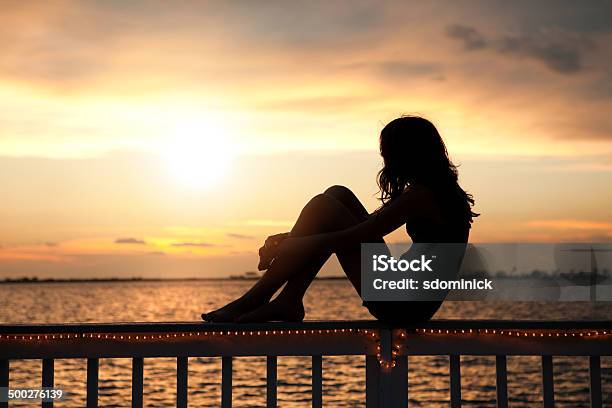 Silueta De Chica Joven Mirando Al Atardecer Foto de stock y más banco de imágenes de Aire libre - Aire libre, Niño, Sentado