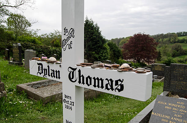 Dylan Thomas headstone, Laugharne Laugharne, UK - May 5, 2014:  Simple wooden cross marking the grave of the great Welsh poet Dylan Thomas in Laugharne, South Wales.  Cockle shells, coins and sweets have bee placed as reminders of his literature. named animal stock pictures, royalty-free photos & images