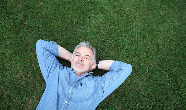 homme mature allongée sur l'herbe. - hands behind head photos et images de collection