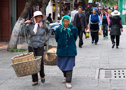 Dali, China - March 23, 2014: Farmers carrying pole walking in Fuxing road of Dali Ancient City, Yunnan Province, China.