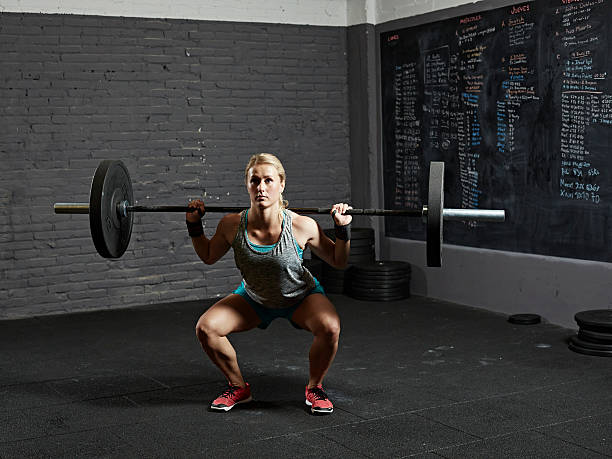 female gym performing back squat - crouching exercising women barbell - fotografias e filmes do acervo