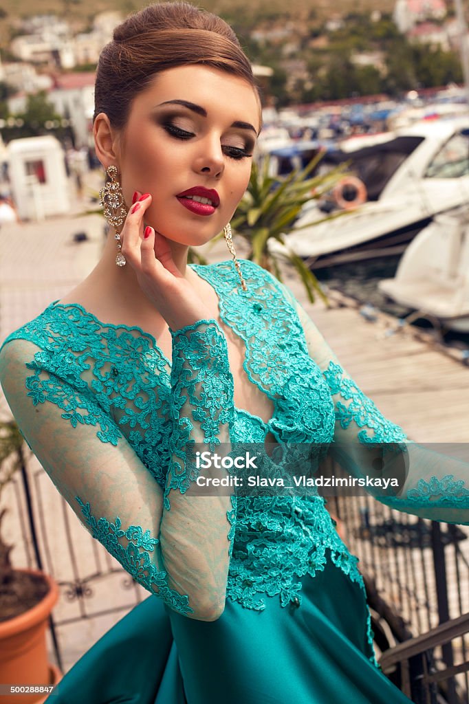 beautiful woman with elegant hairstyle in luxurious silk dress fashion photo of beautiful glamour model with elegant hairstyle in luxurious silk blue dress posing at dock Adult Stock Photo