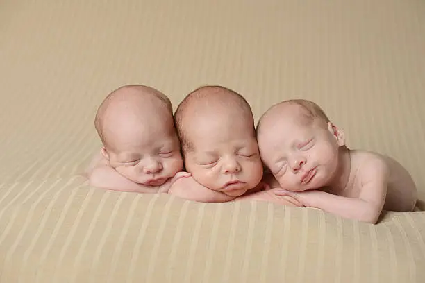 Newborn triplets sleeping peacefully on a blanket. Two are identical.