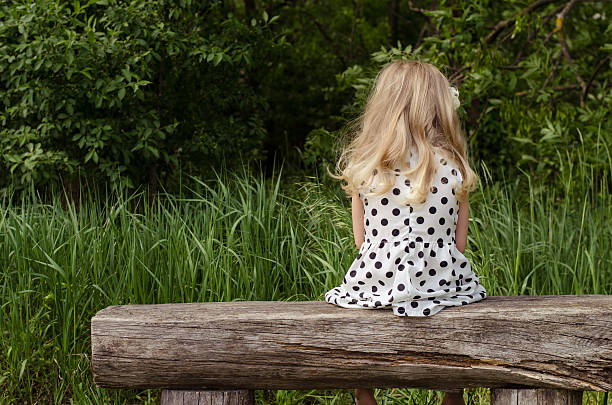 girl with long blond hair sitting in bench and waiting back view
