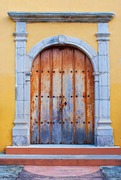 decorative stained red wood gate. carved ornate panels. urban setting with beige stucco finished framed opening. circular columns on square stone base. cobble stone street paving. architecture