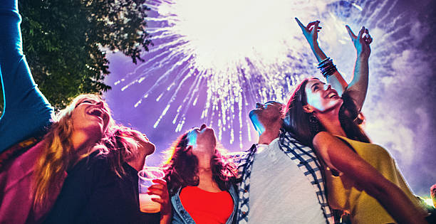 People celebrating with fireworks. Group of young caucasian adults celebrating with fireworks. There are four girls and one guy.Standing side by side and looking at the sky with massive fireworks display behind them. new year urban scene horizontal people stock pictures, royalty-free photos & images