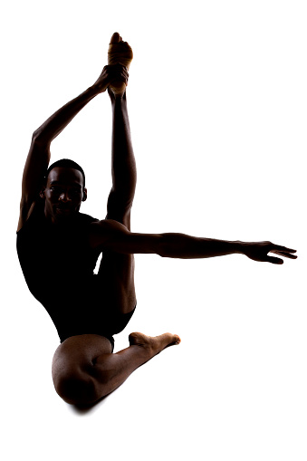 Silhouette of a flexible male dancer posing and balancing on white background.  The fit athletic man is demonstrating his core strength by balancing and flexibility.  The model is backlit for a shadow silhouette effect.  The body forms a letter L.