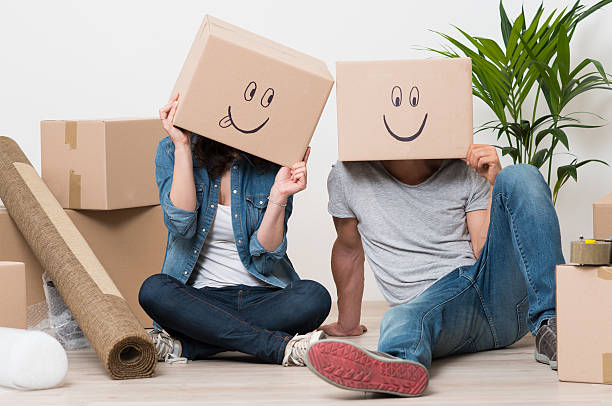 Couple having fun while moving home Couple With Cardboard Boxes On Their Heads With Smiley Face Sitting On Floor After The Moving House irony stock pictures, royalty-free photos & images