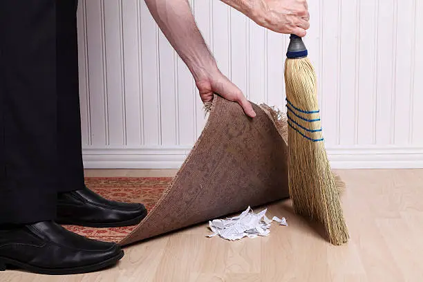 Unrecognizable businessman sweeping a shredded document under the rug