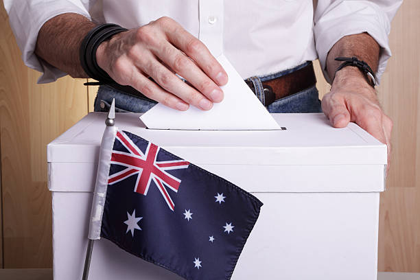 Australians to vote A man inserting a ballot to a ballot box.  Australian flag in front of it. constituency photos stock pictures, royalty-free photos & images