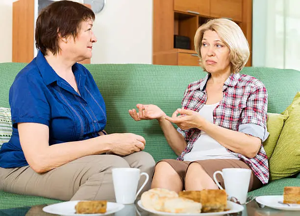 Two sad mature women chating on couch at home