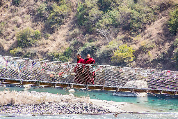 Two monks on the suspension bridge Punakha, Bhutan - March 7, 2014: Two monks are walking over Bhutans longest suspension bridge near the dzong of Punakha. This type of bridge can be found everywhere in Bhutan. Dzongs are fortress like buildings which house a monastery and administrative offices. monastery religion spirituality river stock pictures, royalty-free photos & images