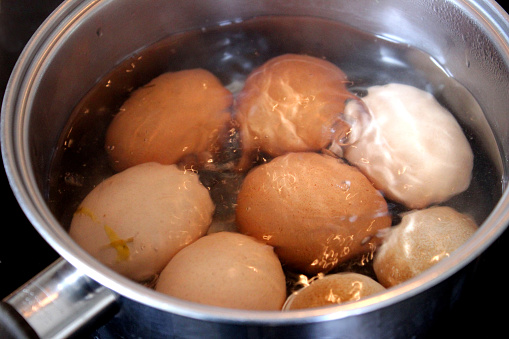 Photo showing some chicken eggs being boiled on the hob, in a stainless steel saucepan of boiling water.  These are organic, free range chicken eggs, which vary greatly in size, shape and colour.
