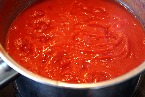 Photo showing some homemade tomato sauce cooking in a saucepan, pictured simmering away and reducing on a low heat.  This is a rich pasta sauce made with tomatoes, tomato puree, finely chopped onion and lots of freshly picked herbs.