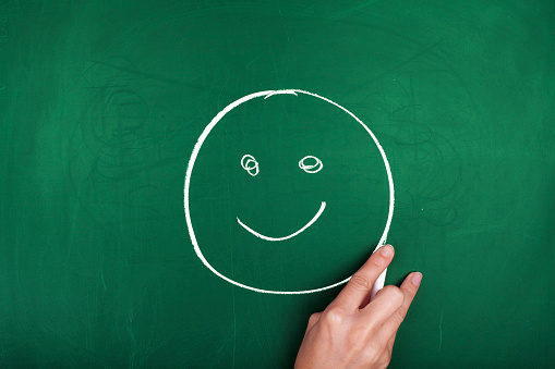 Woman hand drawing smiley face on green blackboard