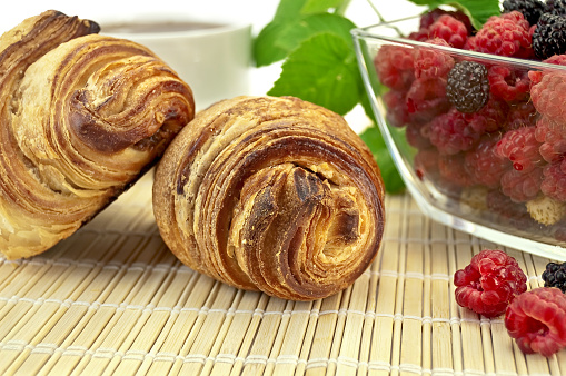 Two croissant, dishes with raspberries, blackberries and strawberries, raspberries green leaf on a bamboo mat