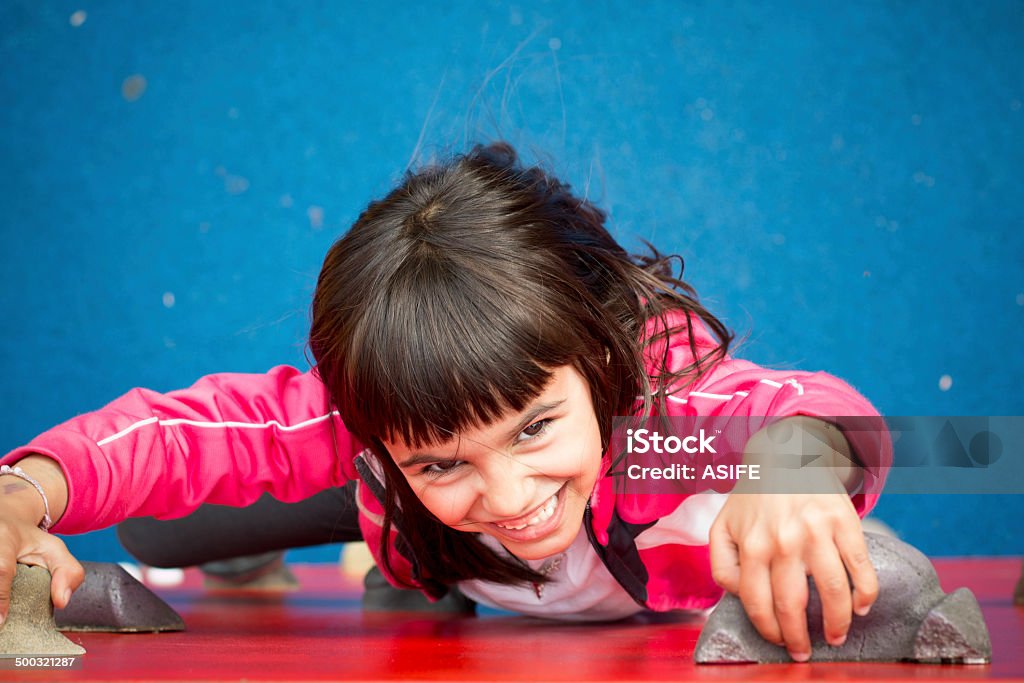 Pretty girl climbing a red wall in a playground Climbing Wall Stock Photo