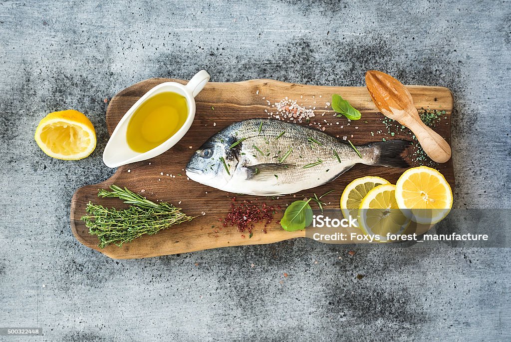 Fresh uncooked dorado or sea bream fish with lemon, herbs Fresh uncooked dorado or sea bream fish with lemon, herbs, oil and spices on rustic wooden board over grunge backdrop, top view Fish Stock Photo