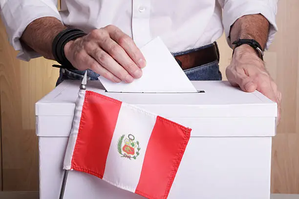 A man inserting a ballot to a ballot box.  Peruvian flag in front of it.