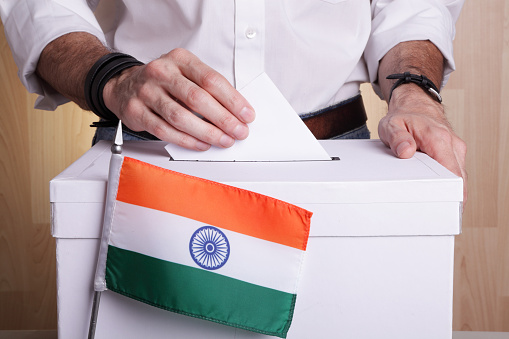 A man inserting a ballot to a ballot box.  Indian flag in front of it.
