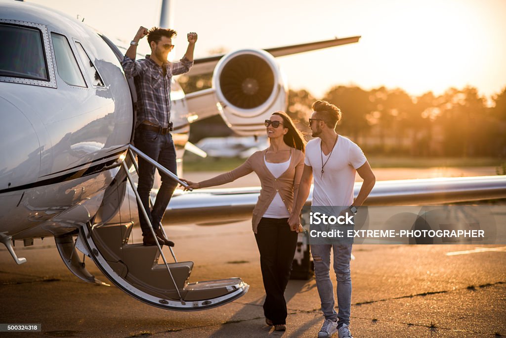 Casual people and private airplane Young casual people with sunglasses standing in front of private jet airplane. Man is holding his girlfriend's hand and another man is standing at the airplane door. Bright sunlight is in the background. Corporate Jet Stock Photo