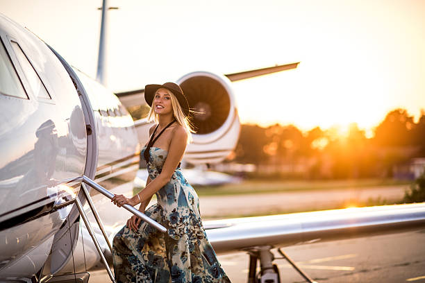 Young blonde woman entering private jet airplane Young blonde elegant woman with hat standing on the stairs of private jet airplane. Bright sunlight is in the background. private jet plane stock pictures, royalty-free photos & images