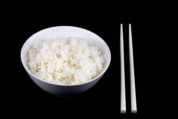 A beautifully composed minimalist food photograph featuring a bowl of fluffy jasmine rice, placed on a fresh banana leaf with wooden chopsticks resting beside it. The natural lighting creates soft shadows, adding depth and contrast to the composition. The clean white background emphasizes the simplicity and elegance of traditional Asian cuisine, making this image ideal for food photography, restaurant branding, culinary blogs, and content related to healthy eating and sustainability.