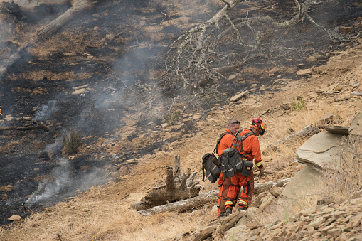 Lake Berryessa, California, USA - June 27, 2015: Two cal fire fire fighters stand by a burning hill side in lake berryessa, california, usa