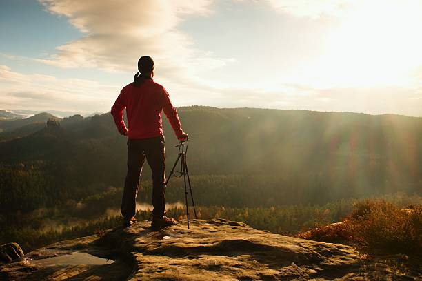Nature photographer with tripod on cliff and thinking. Dreamy landscape