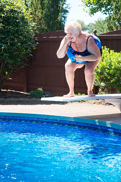 Large lady laughing on diving board Senior woman holds her nose as she prepares to jump off the diving board at a pool fat jump pool stock pictures, royalty-free photos & images