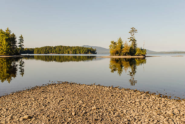 Early Autumn in Maine with trees reflecting in calm waters of late day on Moosehead Lake in Northern Maine.