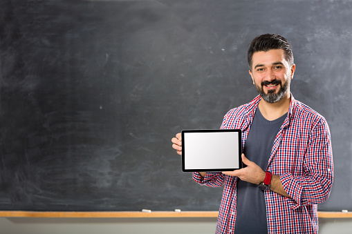 Young man teacher showing blank tablet in classroom
