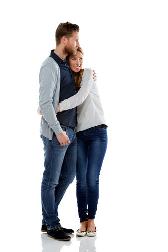 Full length portrait of relaxed couple embracing and looking away over white background.