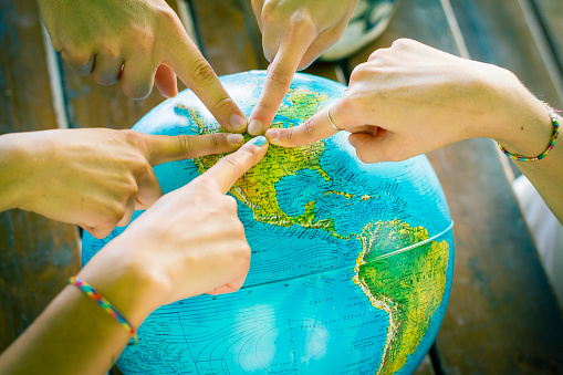 A group of young students (not recognizable) or friends are pointing their fingers on North America map using an earth globe. They are choosing a place for a holiday or are maybe studying geography. Teamwork and Friendship