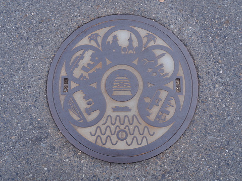 Hakodate, Japan - June 10, 2023: A colorful manhole cover on Kaiko Street in the historic Hakodate Bay Area depicts the outline of the fortress Goryokaku or five-point fort. An illustrated street map lists places in part of the bay area. Rainy spring morning in the port city.
