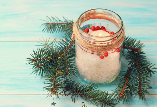  Candle in glass jar, pine boughs, epsom salt, twine. Wooden blue background. Toned.