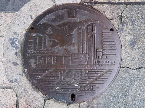 Kobe, Japan - November 19, 2015: A manhole cover in Kobe, Japan. Signs and symbols of important places that represent Kobe engraved on to a manhole along a street in Kobe city.