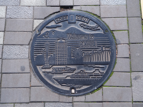 Kobe, Japan - November 20, 2015: A manhole cover in Kobe, Japan. Signs and symbols of important places that represent Kobe engraved on to a manhole along a street in Kobe city.