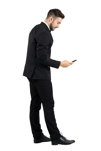 Side view of young businessman in suit typing message on smartphone touchscreen. Full body length portrait isolated over white studio background